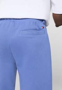 Light blue sweatpants with a soft texture, elastic waistband, and a small back pocket with a branded accent in red, white, and blue.