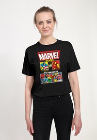 Žena nosící černé tričko Marvel Fighter s postavami Kapitána Ameriky, Iron Mana a několika dalších postav Marvel ve stylu výběru postav z bojové videohry.