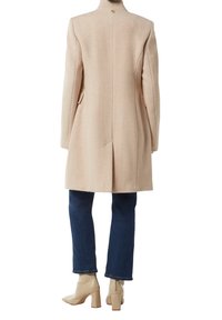 Lichtbeige wollen jas met een op maat gemaakte ontwerp, voorzien van een enkele knoopsluiting bij de nek en zijzakken. Draag het over donkerblauwe jeans en beige laarzen.