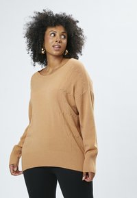  Lys brun sweater med løs pasform, ribbede manchetter og snoningsmønster på den ene side. Blød tekstur og længde under hoften.