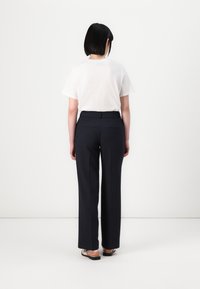 T-shirt en coton blanc et pantalon sur mesure bleu marine avec passants de ceinture. Les pantalons sont dotés de poches arrière et présentent une coupe droite.