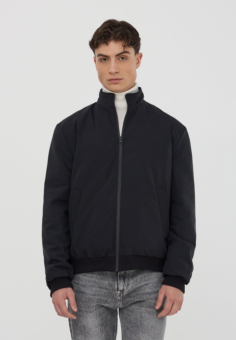 Giacca bomber nera con colletto alto, zip frontale e tasche laterali. Presenta polsini e vita a coste; tessuto morbido al tatto.