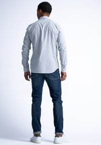 Lichtblauw patroonhemd met lange mouwen, gecombineerd met donkerblauwe jeans en witte sneakers, gezien vanuit de achterkant.