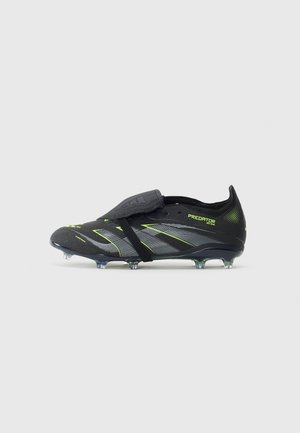 Bota de futebol Adidas Predator em preto e verde néon, com cravos, atacadores cobertos e textura antiderrapante, em um fundo branco liso.