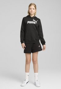 Felpa nera con logo "PUMA" bianco, abbinata a pantaloni corti neri e sneakers bianche. Design semplice, tessuto morbido e vestibilità comoda.