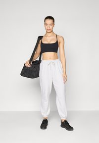 Top sportivo nero, pantaloni da tuta grigi con polsini elasticizzati e sneakers nere; tiene una borsa a tracolla nera. Abbigliamento sportivo semplice e informale.