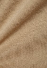 Beiger Strickstoff mit einer glatten Textur, der feine vertikale und horizontale Rippungen aufweist. Weich und dehnbar mit einer gleichmäßigen Farbe.