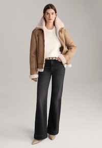 Tawny shearling jack met een witte faux fur kraag, gecombineerd met een gestructureerde witte trui en hoge zwarte uitlopende jeans. Neutrale paarse hakken.