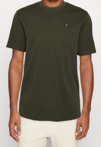 Olivgrön kortärmad t-shirt i bomull, med rund halsringning och en liten emblem på bröstet. Slät textur och avslappnad passform.