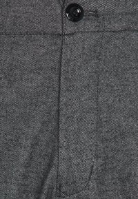 Šedá texturovaná látka s knoflíkovým zapínáním a švy. Obsahuje boční kapsu a jemný herringbone vzor, který ukazuje odolnost.