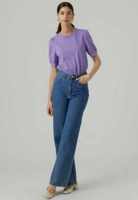 Šviesiai violetinė trumpa rankovė maikutė su pūstomis petnešomis, derinama su aukštu liemeniu tiesiomis mėlynomis džinsomis. Lygiais kulnais bežinės spalvos bateliai užbaigia įvaizdį.