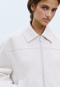 Veste en polaire rose clair avec col et fermeture éclair. Dotée de poches latérales et d'une finition douce et texturée.