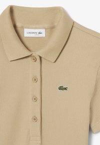 Polo shirt a coste beige con colletto classico, chiusura a tre bottoni e logo coccodrillo ricamato verde sul petto.