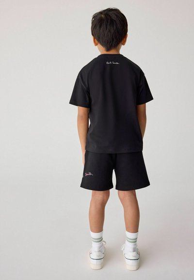 Svart t-shirt och shorts-set i mjukt tyg. Notabla egenskaper inkluderar färgglad "Paul Smith" brodyr och vita sneakers med gröna detaljer.