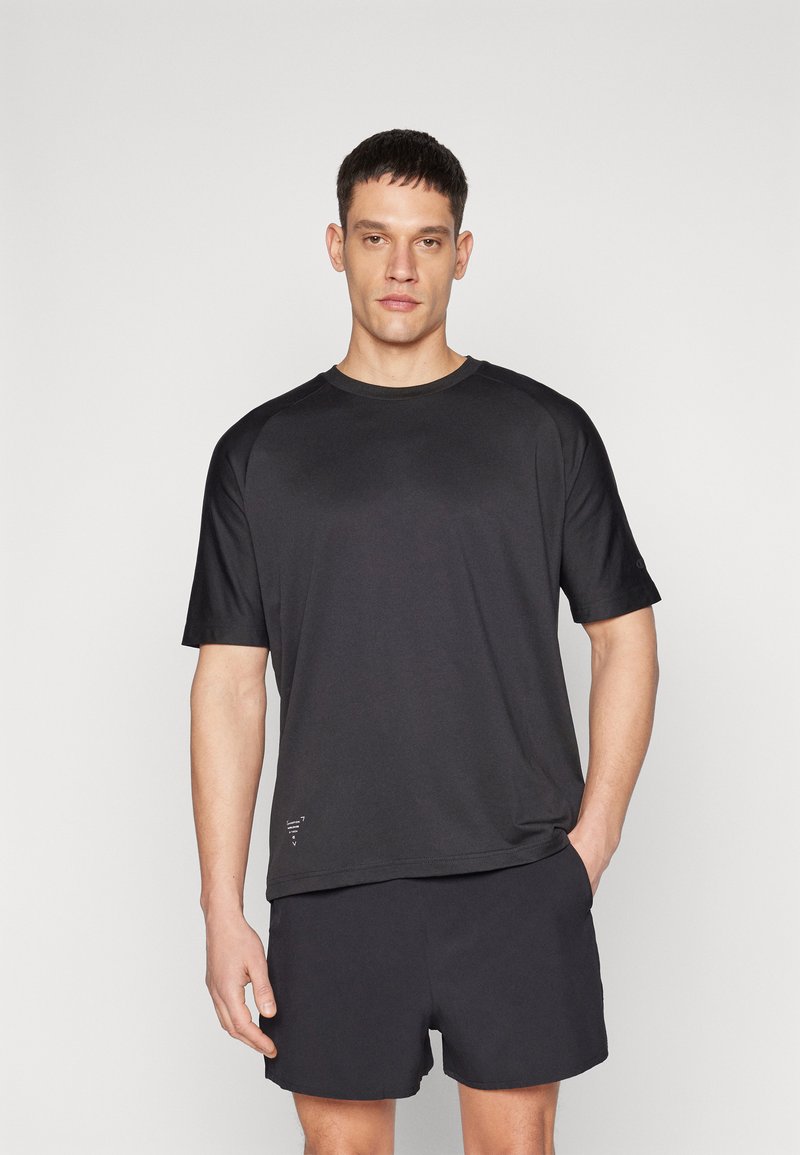 Svart sport t-skjorte og shorts sett. T-skjorten har rund hals, korte ermer og en glatt tekstur. Subtil merkevaredetalj ved kanten.