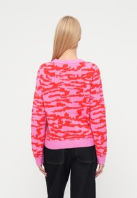 Knit sweater with a pink and red camouflage pattern, round neckline, ribbed cuffs, and hem. Made from a soft, textured material.