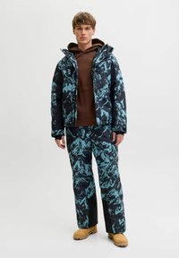 Veste et pantalon de neige en bleu marine avec un motif abstrait turquoise. Fabriqués en tissu texturé brillant. Comprend une capuche et des poches.