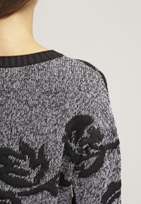 Czarny i biały sweter z dzianiny z teksturowanym wzorem dużych czarnych róż. Żebrowany dekolt i teksturowana tkanina w luźnym kroju.