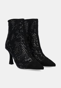 Botas negras hasta el tobillo con parte superior de malla texturizada, punta afilada y detalles de ante. Presentan un tacón alto y delgado y un patrón geométrico.