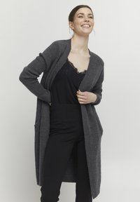Lång, mörkgrå cardigan med öppen framsida, ribbade ärmslut och fickor, lagd över ett svart spetslinne och svarta byxor. Mjuk textur.