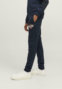 Marineblå sweatpants med elastisk talje, sidelommer og et detaljeret logo-patch. Parret med hvide sneakers for kontrast.