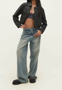 Černá krátká kožená bunda se dvěma předními kapsami, doplněná volnými světle modrými džínami a černými robustními botami na platformě.