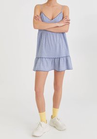 Vestido sin mangas a rayas azul y blanco con un dobladillo con volantes, confeccionado con tela ligera; combinado con calcetines amarillos y zapatillas blancas.