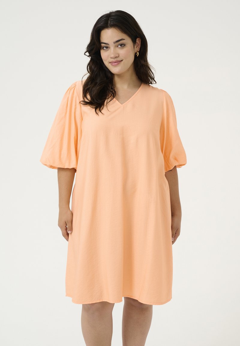 Robe A-line couleur pêche en tissu léger. Présente un col en V et de courtes manches bouffantes avec une texture lisse. Design simple, sans motifs.