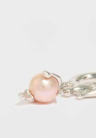 Rozā pērle, kas ietverta neregulārā sudraba metāla ietvarā, pievienota sudraba apaļam aizdares mezglam uz baltas fona.