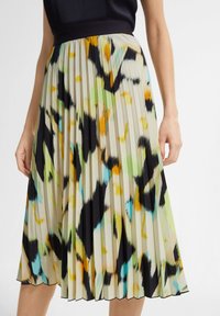 Falda midi plisada hecha de tejido ligero con un patrón abstracto en verde, naranja, negro y azul sobre un fondo beige.