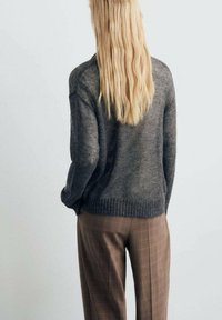 Pull en tricot gris à coupe ample, avec un ourlet côtelé et une texture. Pantalons à carreaux bruns avec une coupe droite.