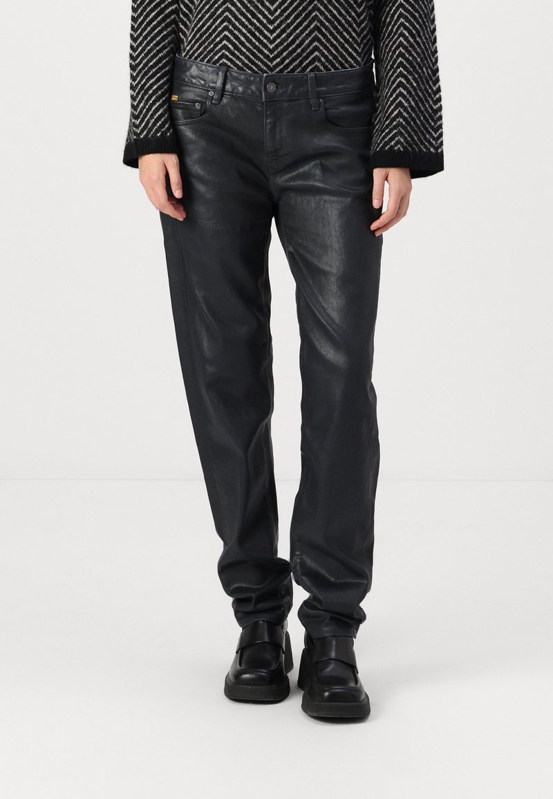 Pantalones de cuero negro con una textura ligeramente brillante, diseño de cinco bolsillos y cintura ajustada. Combinados con botas negras gruesas.