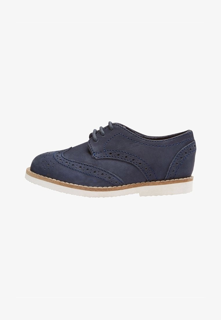 Chaussure Oxford en cuir bleu marine avec détails brogue, semelle blanche, piqûre beige et fermeture à lacets, vue de profil.
