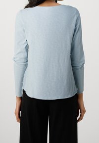 Ljusblå långärmad topp i mjukt tyg med rundad halsringning, subtil textur och en något böjd nederkant baktill.