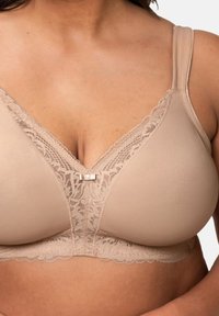 Beige podprsenka s krajkovým zdobením na výstřihu, nastavitelné ramínka a malá dekorační mašle uprostřed tvaru V.