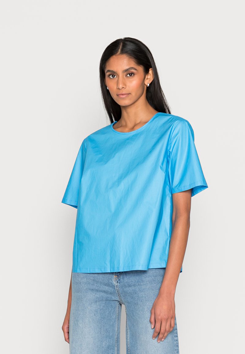 T-shirt de manga curta azul-claro feito de material liso, com um decote redondo e um corte solto e boxy, combinado com jeans de denim claro.