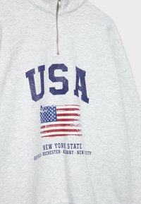 Sweat-shirt zippé gris clair avec grand texte bleu "USA", drapeau américain usé et "New York State" avec noms de villes en dessous.
