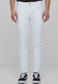 Jeans ajustados blancos con un diseño clásico de cinco bolsillos, cierre de botón y un ligero estiramiento; combinados con zapatillas en blanco y negro.