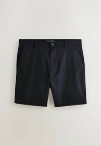Shorts noirs sur mesure longueur genou avec bouton sur le devant, passants de ceinture et poches latérales sur fond beige.