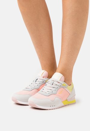 Nohy v růžových, šedých a žlutých teniskách Pepe Jeans s tkaničkami, zobrazené na bílém pozadí.