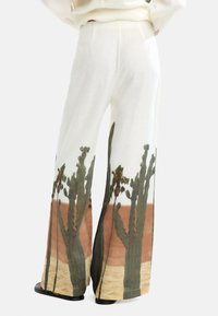 Lnianowe spodnie z szerokimi nogawkami z nadrukiem kaktusa w odcieniach zieleni i brązu, na białym tle o subtelnej teksturze. Zapewniają luźny krój.