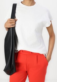 Vit bomull T-shirt med kort ärm, kombinerad med röda skräddarsydda byxor. En texturerad svart läderväska hängande över axeln.