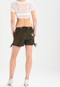 Brązowe zamszowe szorty o dopasowanym kroju, z wiązaniami po bokach i kwiatowym haftem na tylnej kieszeni, zestawione z białą koronkową bluzką typu crop top.