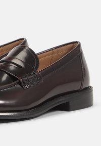 Tumman burgundin väriset nahka loaferit, joissa on sileä pinta, kudottu yksityiskohta ja tasapohja, suunniteltu helppoa pukemista varten.