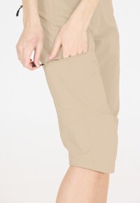 Beige zip-off cargoshorts med sidfickor, tillverkade av lätt material. Har justerbara dragkedjor och en skräddarsydd passform för enkel rörelse.