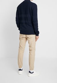 Marinblå stickad tröja med strukturerade ränder, i kombination med ljusbeige tapered byxor och vita sneakers med marinblå detaljer.