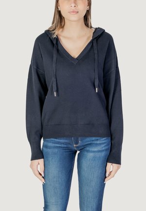 Felpa nera con scollo a V, cordini e polsini a coste. Tessuto morbido, vestibilità rilassata, abbinata a jeans blu aderenti.