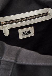 Černý vnitřek látkové tašky s bílým zipem a koženými doplňky. U zipu je viditelná značka s nápisem „KARL LAGERFELD“.