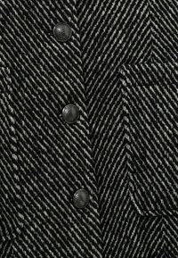 Černobílá látka s rybí kostí a texturovaným povrchem. Obsahuje velké černé knoflíky a boční kapsu.