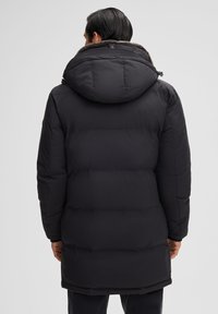 Zwarte gewatteerde jas met een grote capuchon en faux bont voering, voorzien van een doorgestikt design en verstelbare manchetten voor warmte en comfort.